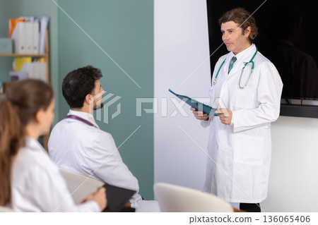 Male doctor holding paper sheets explaining medical topic to students 136065406