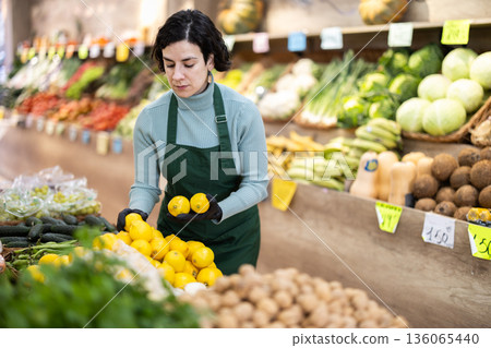 Adult woman seller puts lemons on display Adult woman seller puts lemons on display 136065440