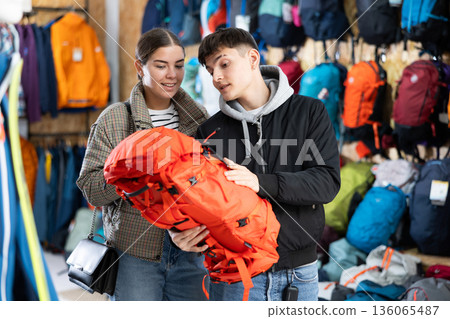Young married couple in winter clothes chooses a durable backpack for a winter hike in tourist equipment store 136065487