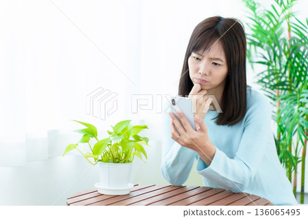 A housewife using a smartphone with a troubled look on her face 136065495
