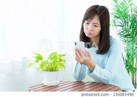 A housewife using a smartphone with a troubled look on her face 136065496