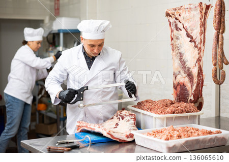 Happy female butcher sawing big chunk of beef meat in meat section of supermarket 136065610
