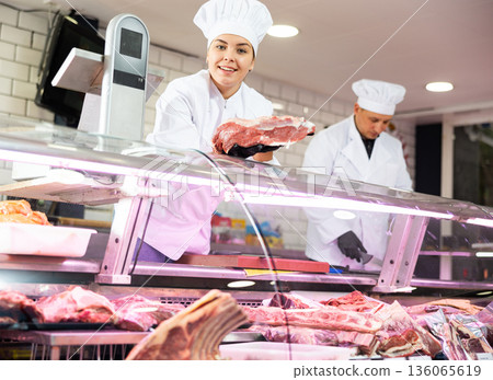 Happy female butcher holding big chunk of beef meat in meat section of supermarket Happy female butcher holding big chunk of beef meat in meat section of supermarket 136065619