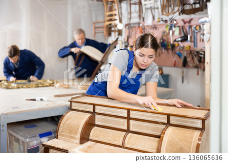Young woman polishes tabletop of old chest of drawers with rounded drawers with soft cloth 136065636