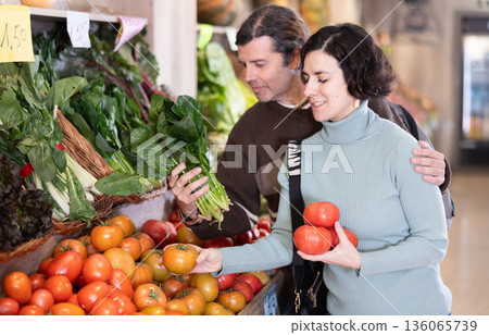 Married couple selects fresh bell peppers, tomatoes and other vegetables at supermarket counter Married couple selects fresh bell peppers, tomatoes and other vegetables at supermarket counter 136065739