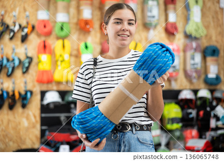 Young girl chooses and buys climbing rope for trip to the mountains in sports equipment store 136065748