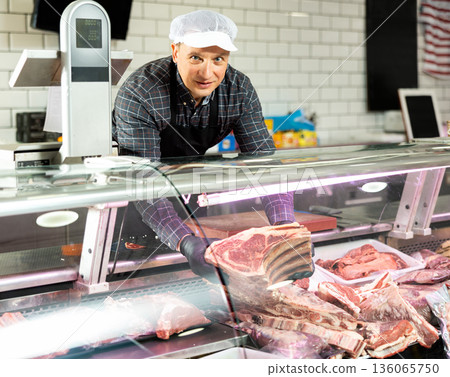 Confident male butcher showing a big piece of beef ribs in butchery Confident male butcher showing a big piece of beef ribs in butchery 136065750