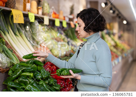 Adult woman chooses peppers in vegetable shop 136065781