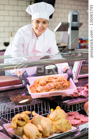 Young woman puts chicken meat in showcase 136065795