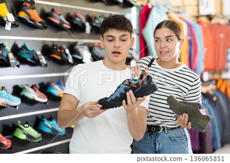 Guy with girlfriend, view specialized shoes in store, near showcase with summer trecking cross-shoes 136065851