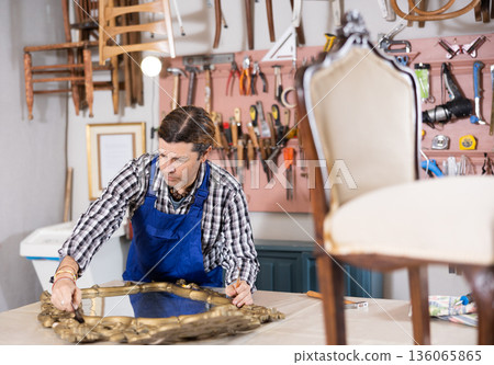 Male furniture maker diligently working on vintage mirror in workshop 136065865