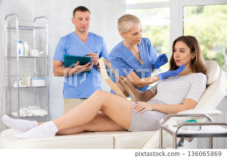 Plastic surgeon and nurse consulting young woman before facelift operation in clinic Plastic surgeon and nurse consulting young woman before facelift operation in clinic 136065869