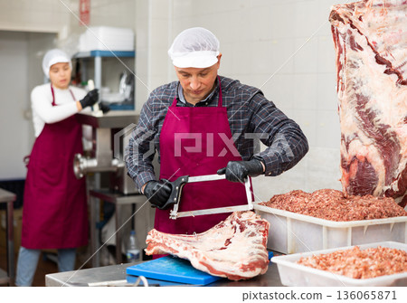 Smiling male butcher sawing large chunk of beef meat in butcher shop Smiling male butcher sawing large chunk of beef meat in butcher shop 136065871