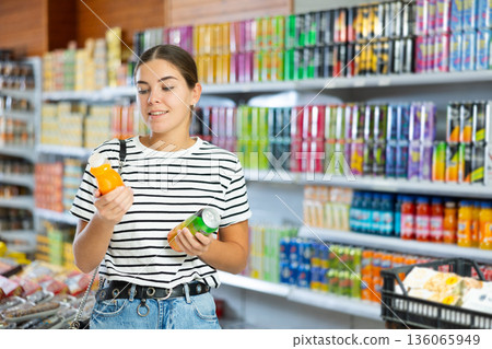 Girl attentively chooses which drink to buy in grocery hypermarket Girl attentively chooses which drink to buy in grocery hypermarket 136065949