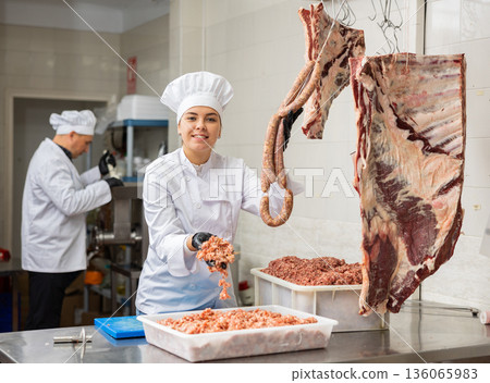 Female butcher offering raw sausages made of fresh forcemeat 136065983