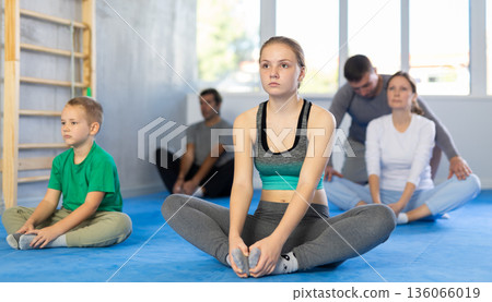 Family during group workout with trainer in gym performs stretching of muscles of inner thigh by performing butterfly exercise Family during group workout with trainer in gym performs stretching of muscles of inner thigh by performing butterfly exercise 136066019