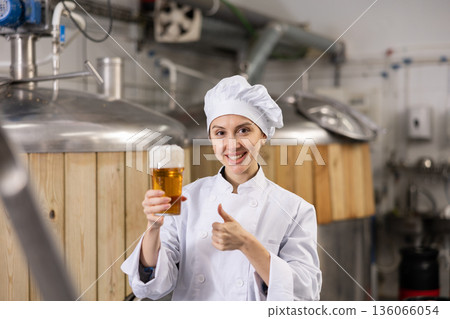 Female brewer showing thumbs up while holding glass of beer Female brewer showing thumbs up while holding glass of beer 136066054