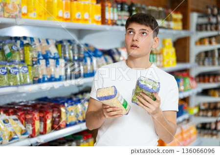 Guy pondering choice between yellow split chickpeas and green peas in grocery store Guy pondering choice between yellow split chickpeas and green peas in grocery store 136066096