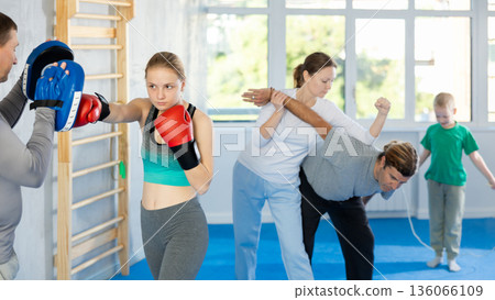 Teen girl works out strength and speed of boxing punch mitts with help of partner in boxing paws 136066109