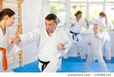 Focused woman in kimono practices combat technique of punching and blocking with trainer at family martial arts class 136066141