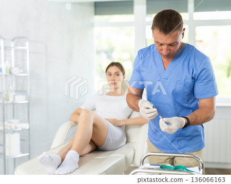Male doctor performs intra-articular injection treatment of knee bursitis to woman patient 136066163
