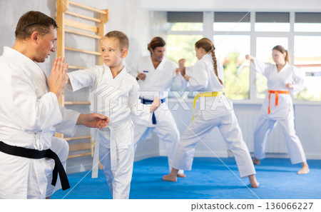 Boy at group training in gym practice karate punch block technique with trainer 136066227