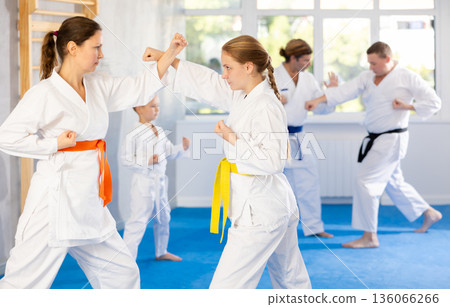 Teen girl sparring with woman at group training in gym practice karate punch block technique Teen girl sparring with woman at group training in gym practice karate punch block technique 136066266