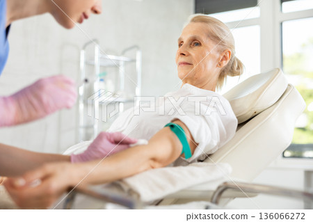 Old woman patient having vein injection lying on clinical chair 136066272