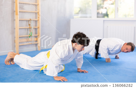 Teenage boy and middle-aged man wearing kimono standing in plank position Teenage boy and middle-aged man wearing kimono standing in plank position 136066282