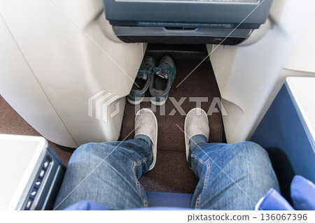 Inflight business class passenger with ample leg room replaces shoes with disposable slippers during flight for comfort travel 136067396