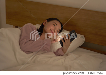 A woman using a smartphone in bed A woman using a smartphone in bed 136067562