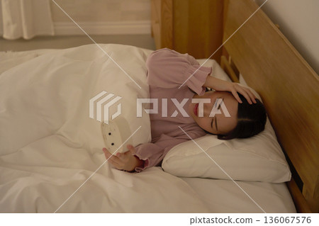 深夜，一位女士躺在被褥裡看著時鐘 136067576