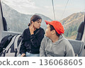 Two children ride a cable car in the mountains. A young Asian boy with a red cap and a young Asian girl smile together. Scenic mountain view in the background 136068605