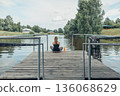 woman sitting cross-legged on wooden dock over calm river, wearing sportswear, back view, summer greenery, countryside houses, meditation, morning ritual, nature therapy 136068629