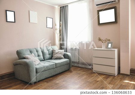 Cozy hotel room with a light pink wall, a green sofa, and a white dresser. Natural light streams through a large window, creating a welcoming atmosphere. Cozy hotel room with a light pink wall, a green sofa, and a white dresser. Natural light streams through a large window, creating a welcoming atmosphere. 136068633