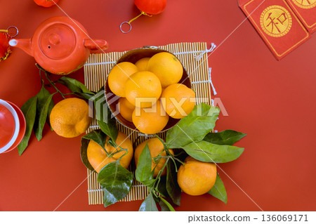 Fresh oranges sits next to teapot on red table with Chinese festive Lunar New Year decorations around. 136069171
