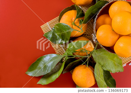 Oranges fruits, green leaves are placed on bamboo mat on red table in simple Chinese festive Oranges fruits, green leaves are placed on bamboo mat on red table in simple Chinese festive 136069173