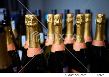 Rows of champagne bottles, gold foil, pink labels, closeup retail shelf, blurred background, warm highlights, premium texture, celebratory mood, event preparation, upscale party Rows of champagne bottles, gold foil, pink labels, closeup retail shelf, blurred background, warm highlights, premium texture, celebratory mood, event preparation, upscale party 136069246
