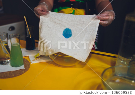 Hands apply blue dye meticulously. Closeup of textile dye application in workshop. An artistic depiction of careful blue dyeing on white textile in creative environment Hands apply blue dye meticulously. Closeup of textile dye application in workshop. An artistic depiction of careful blue dyeing on white textile in creative environment 136069588