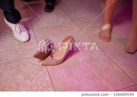 Footwear left behind. Guests dance barefoot amidst lights. Barefoot dancers enjoy night under luminous illumination. Lively scene with scattered shoes and dancing without footwear 136069599
