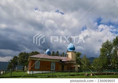 Calm pastoral setting with rustic architecture and natural beauty. Idyllic countryside landscape showcasing historic church surrounded by lush greenery and cloudy skies 136069605