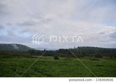 Cloudy misty landscape. Silent countryside under heavy gray clouds and morning dew. Peaceful scene with mist rolling over fields and distant hills beneath heavy cloud cover 136069606