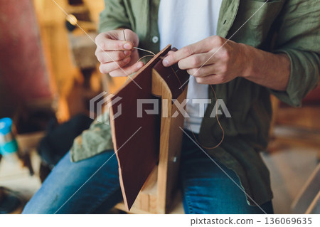 Handcrafted leather journal. Focused image of homemade leather book being handcrafted. Intimate view of skilled craftsman sewing waxed thread onto brown leather journal Handcrafted leather journal. Focused image of homemade leather book being handcrafted. Intimate view of skilled craftsman sewing waxed thread onto brown leather journal 136069635