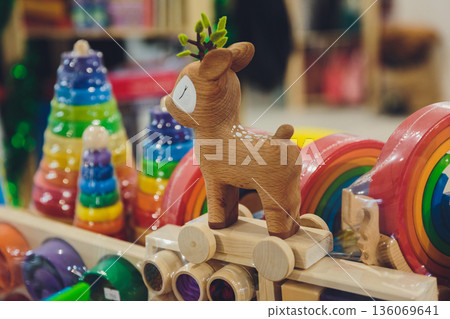 Crafted wooden stag surrounded by playful colorful toy accessories for display. Artisan carved deer amidst multicolored wooden train and stacking toys in cozy shop setting 136069641