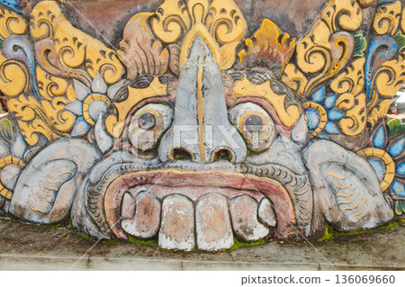 Decorative ancient mask, Ornate stone face with details, Weathered guardian mask with intricate features, Closeup of historic ceremonial stone mask highlighting colors and textures 136069660