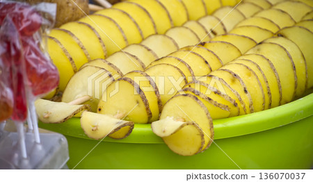Rows of spiral-cut potatoes on sticks await frying, displayed at a street food stand. Rows of spiral-cut potatoes on sticks await frying, displayed at a street food stand. 136070037