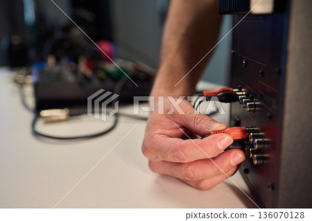 Setting up audio connection professionally, Attaching sound cable to subwoofer in studio, Closeup of hands securing audio cable into subwoofer in recording studio setting Setting up audio connection professionally, Attaching sound cable to subwoofer in studio, Closeup of hands securing audio cable into subwoofer in recording studio setting 136070128