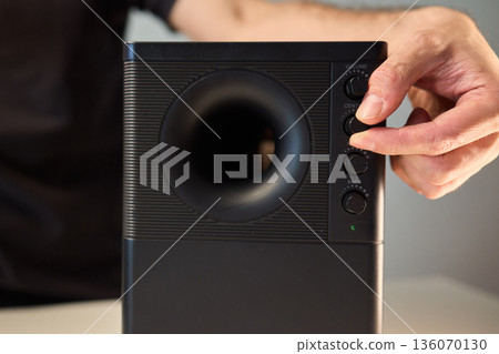 Adjusting bass knob in listening space, Technician modifies subwoofer settings in cozy setup, Close examination of audio equipment controls under warm lighting conditions 136070130