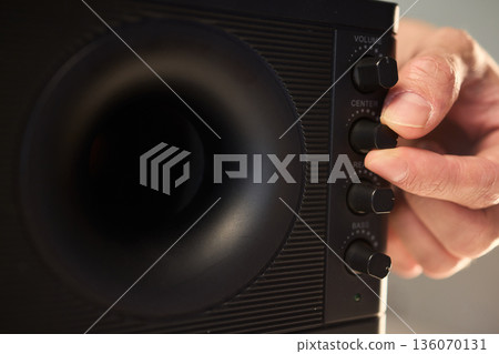 Adjusting bass knob in listening space, Technician modifies subwoofer settings in cozy setup, Close examination of audio equipment controls under warm lighting conditions 136070131