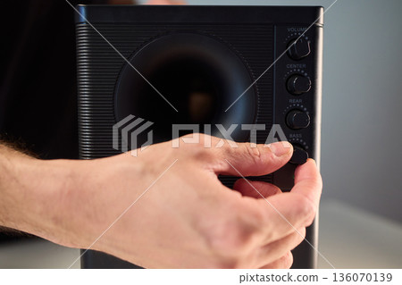 Adjusting bass knob in listening space, Technician modifies subwoofer settings in cozy setup, Close examination of audio equipment controls under warm lighting conditions Adjusting bass knob in listening space, Technician modifies subwoofer settings in cozy setup, Close examination of audio equipment controls under warm lighting conditions 136070139